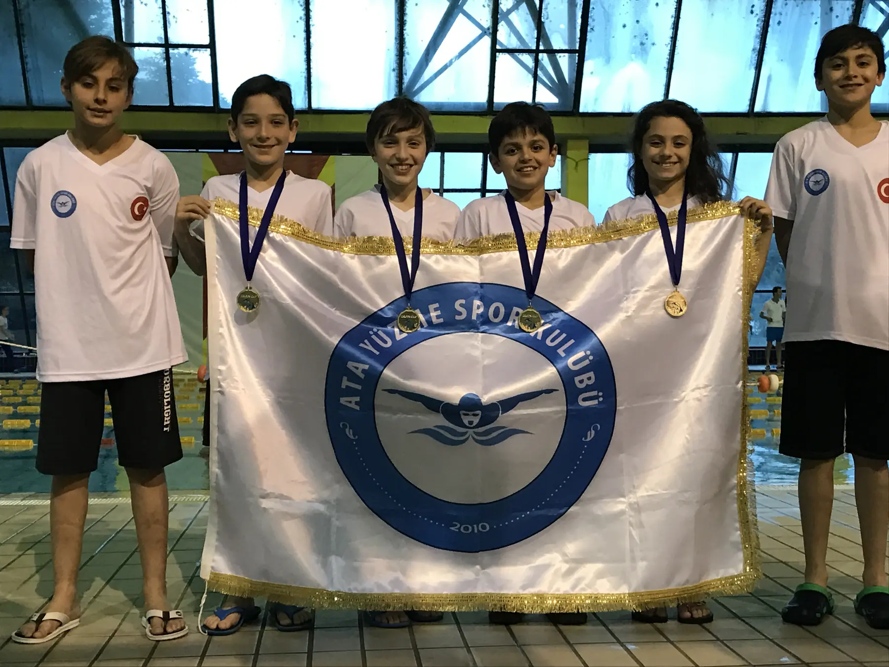 Medal-winning Ata Swimming athletes with their club flag